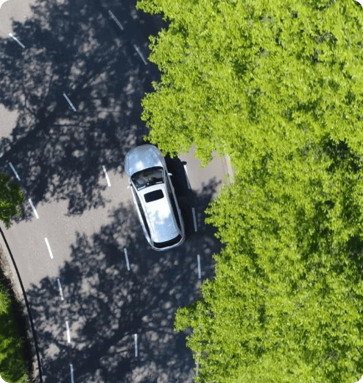Vue aérienne d'une voiture circulant près de la végétation luxuriante, mettant en évidence l'importance de la conduite écoresponsable face aux défis climatiques.