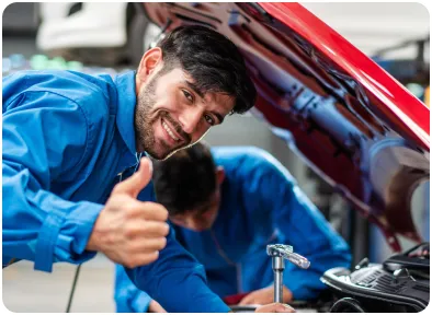 Technicien automobile souriant donnant son approbation avec un pouce levé, après une intervention réussie sur un véhicule.